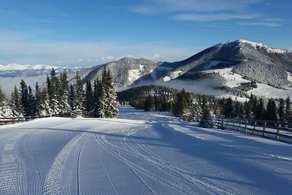 Blick von der verschneiten Piste auf die verschneiten Berge