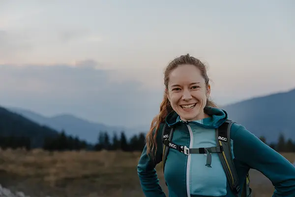 Wanderin schaut in die Kamera und dahinter befindet sich das Bergpanorama.