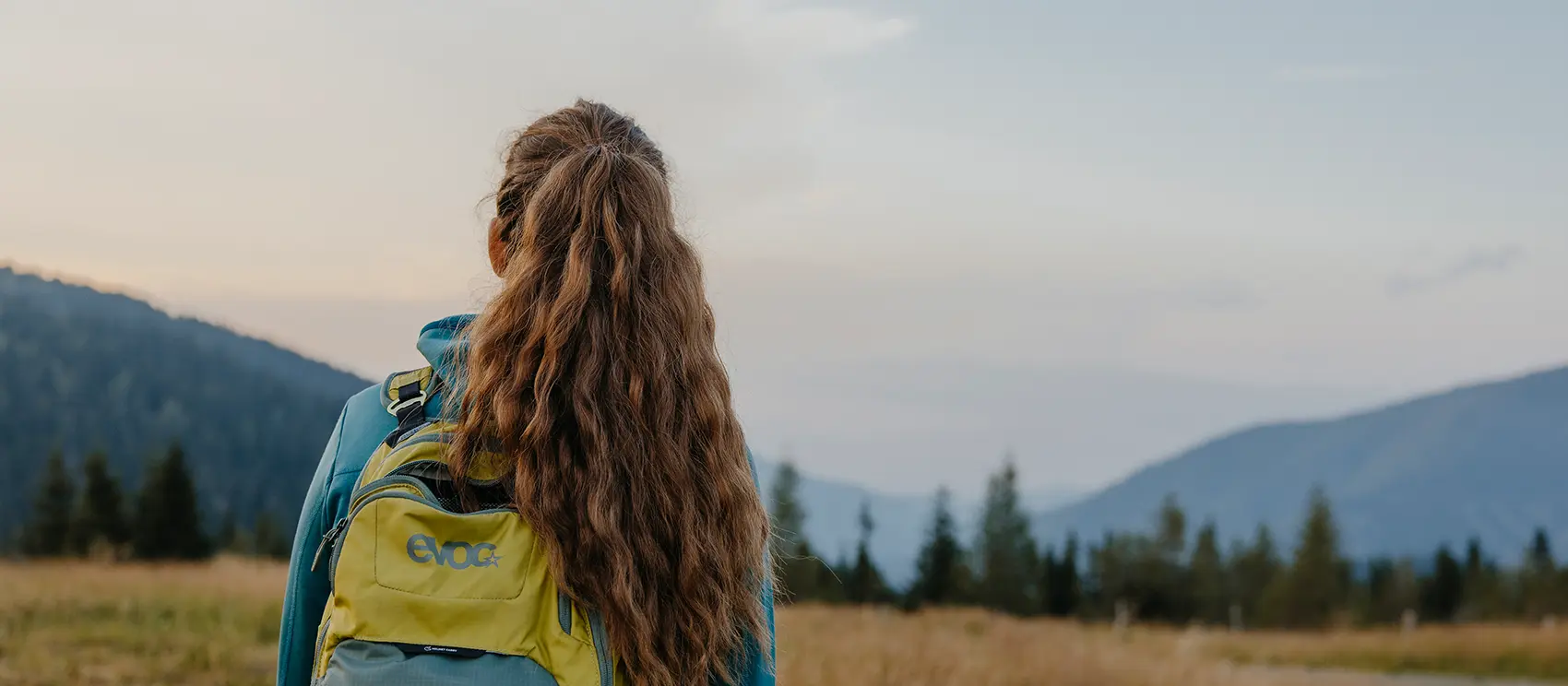 Ein junge Frau von hinten mit Rucksack schaut in die herrliche Bergwelt.